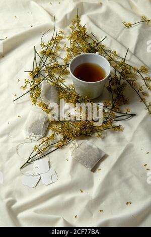 Sopra la tazza bianca con il tè e le tessere posizionate sopra letto con bouquet di fiori gialli per una deliziosa colazione in letto Foto Stock