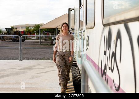 Forte soldato femminile che guarda la macchina fotografica mentre si è in piedi vicino a grugnoso veicolo militare in campagna Foto Stock