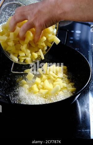 Dall'alto dello chef raccolto che versa fette di patate da setaccio per padella con olio bollente in cucina moderna Foto Stock