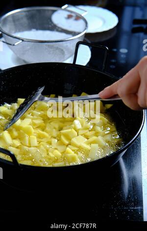 Dall'alto dello chef raccolto che versa fette di patate da setaccio per padella con olio bollente in cucina moderna Foto Stock