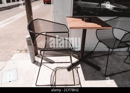 Cafe Terrace con moderne sedie in metallo e tavolo in legno pavimentazione in cemento di strada alla luce del sole Foto Stock