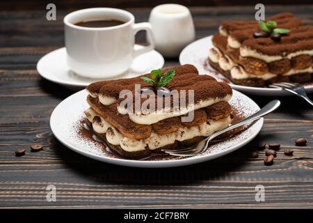 Due porzioni di dessert classico tiramisù, tazza di caffè e latte o crema su sfondo di legno Foto Stock