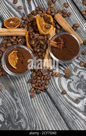 Chicchi di caffè. Caffè macinato in contenitori e spezie. Su una superficie di tavole di pino spazzolato dipinte in bianco e nero. Foto Stock