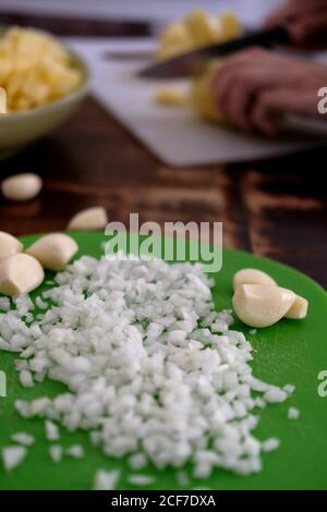 Colpo verticale di cipolle tagliate a dadini e spicchi d'aglio interi un tagliere verde Foto Stock