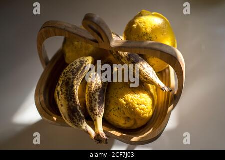 Dall'alto di banane fresche mature e limoni in legno cestino posto sul tavolo in cucina leggera Foto Stock