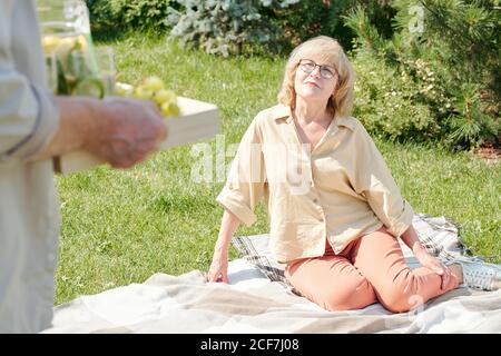 Uomo anziano irriconoscibile che porta cibo e limonata a sua moglie aspettandolo per iniziare il picnic sul prato Foto Stock