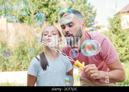 Gioioso padre che si diverte con la sua bella figlia soffiando sapone bolle all'aperto Foto Stock