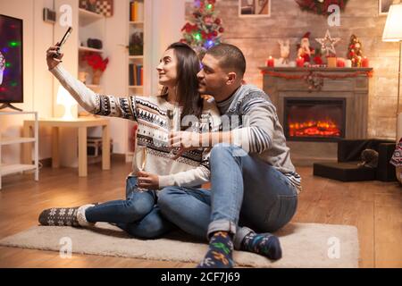 Felice ragazza che prende un selfie con il suo ragazzo il giorno di natale. Gatto dormendo sullo sfondo. Foto Stock