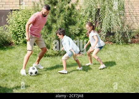 Moderno padre che gioca a calcio con suo figlio e sua figlia prato in cortile Foto Stock