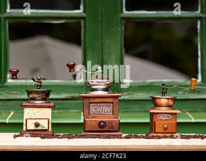 Mulini manuali d'epoca con chicchi di caffè posti su un tavolo di legno di fronte ad una finestra di un'accogliente caffetteria Foto Stock