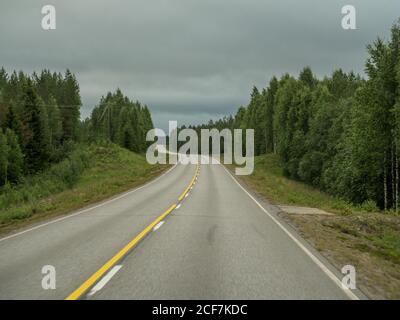 Strada asfaltata vuota attraverso la foresta verde in estate nuvoloso giorno In Finlandia Foto Stock