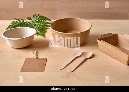 Confezione per alimenti in cartone riciclabile e forchetta e coltello in legno posizionati su tavolo con foglia di felce Foto Stock