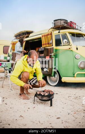Uomo in scatola cucina su campeggio stufa accanto al mini van parcheggiato Foto Stock