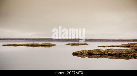 Vista pittoresca del lago e della costa con scogliera di pietra e. Erba secca in Islanda Foto Stock