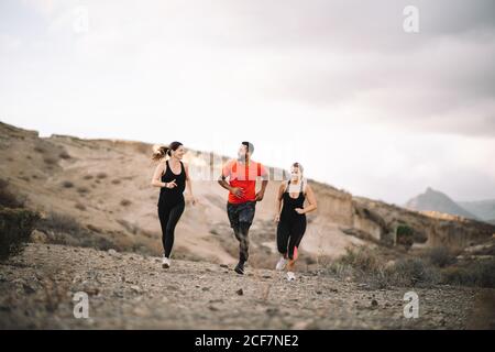 Diversi amici maschili e femminili vestiti di running sportivo al mattino con scogliera di sabbia sullo sfondo Foto Stock