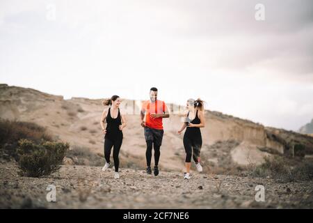 Diversi amici maschili e femminili vestiti di running sportivo al mattino con scogliera di sabbia sullo sfondo Foto Stock