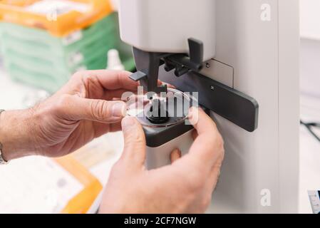Mani di optometista anonimo utilizzando uno strumento professionale per realizzare l'obiettivo per occhiali in laboratorio Foto Stock
