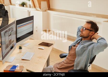 Uomo maturo seduto sul suo posto di lavoro e guardando il computer monitora il lavoro sul software in ufficio Foto Stock