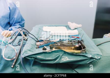 Da sopra medic di raccolto in uniforme mettendo le forbici sul vassoio con utensili chirurgici in acciaio inox in sala operatoria Foto Stock