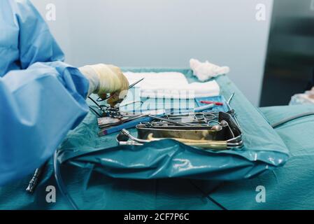 Da sopra medic di raccolto in uniforme mettendo le forbici sul vassoio con utensili chirurgici in acciaio inox in sala operatoria Foto Stock