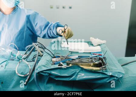 Da sopra medic di raccolto in uniforme mettendo le forbici sul vassoio con utensili chirurgici in acciaio inox in sala operatoria Foto Stock