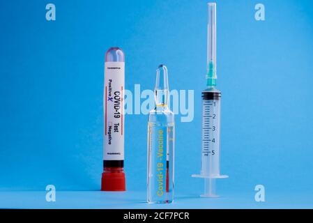 Fiala con vaccino del coronavirus e siringa posta vicino alla provetta con Campione di sangue per il test COVID 19 con segno positivo in sfondo blu Foto Stock