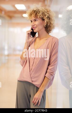 Giovane donna sorridente ha una conversazione sul telefono cellulare mentre in piedi in ufficio Foto Stock