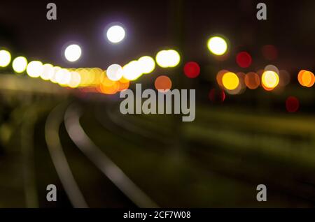 Sfondo sfocato con sagome di binari ferroviari e illuminazione notturna della stazione ferroviaria