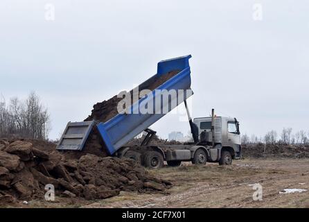 Il dumper scarta il suo carico di sabbia e terreno sul cantiere per la costruzione di strade o per lavori di fondazione. Trasporto di merci sfuse. Trasporto Foto Stock