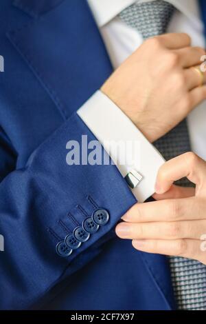 Lo sposo o l'uomo d'affari allacciano il cucciolo sul polsino della camicia che indossa il vestito blu. Messa a fuoco morbida Foto Stock