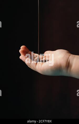 Appetitoso cioccolato caldo fuso che viene versato su una persona non riconoscibile tagliata mano posta su sfondo scuro Foto Stock