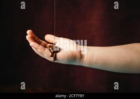 Appetitoso cioccolato caldo fuso che viene versato su una persona non riconoscibile tagliata mano posta su sfondo scuro Foto Stock