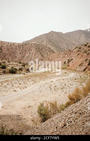 Vuota strada sterrata curva che attraversa la valle del deserto asciutto tra Montagne nella campagna marocchina Foto Stock