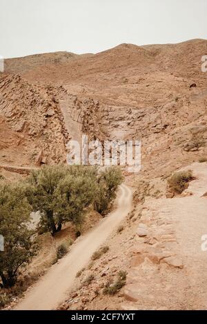 Vuota strada sterrata curva che attraversa la valle del deserto asciutto tra Montagne nella campagna marocchina Foto Stock