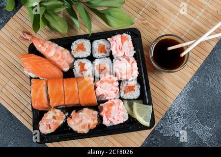 Scatola di consegna sushi con maki, gunkan, sushi nigiri e bastoni di legno con soia. Background del concetto di consegna di cibo Foto Stock