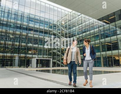 Il corpo pieno ha deliziato i colleghi sorridendo e guardandosi l'un l'altro mentre camminate all'esterno dell'edificio contemporaneo dopo il lavoro Foto Stock