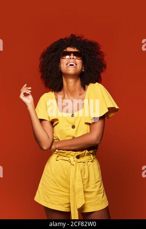 Moderna giovane donna nera con acconciatura afro che si posa sorridendo alla fotocamera su sfondo rosso brillante Foto Stock