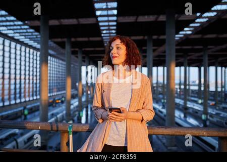 Giovane donna sorridente che tiene il telefono alla stazione Foto Stock