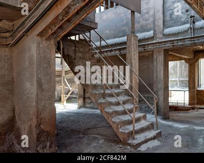 Scalinata in cemento con ringhiere arrugginite che conducono all'ingresso posteriore a officina invecchiata sul territorio di fabbrica abbandonata a freddo mattina invernale Foto Stock