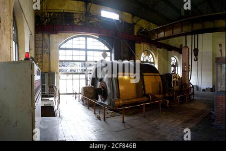 Macchina circolare industriale con meccanismo metallico che si trova all'interno deserted senza proprietà laboratorio industriale dilatato con pareti leggere e grandi finestre ad arco Foto Stock