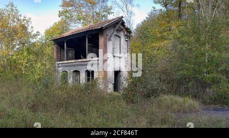 Shabby rovinato abbandonato due piani casa in mattoni senza porta e tetto rotto che si trova tra alberi verdi in giorno nuvoloso in campagna Foto Stock