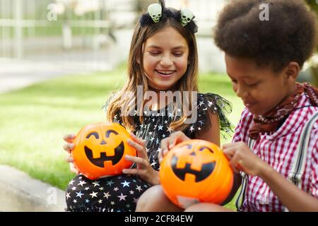 Felici i bambini che si siedono all'aperto e che guardano i sacchetti delle zucche pieni di dolci Foto Stock