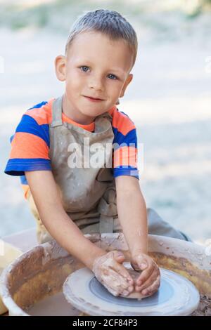 Piccolo ragazzo sorridente prodotto su vasaio ruota pentola. Mani di giovane vasaio, creando un vaso di terra sul cerchio, primo piano Foto Stock