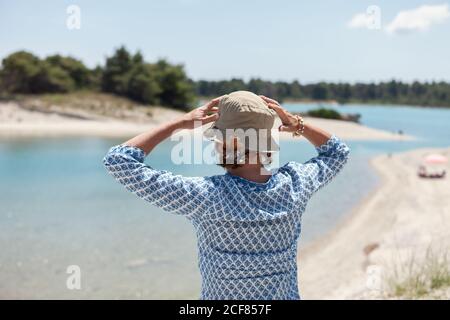 Vista posteriore della donna in cappello con le mani sollevate godendo il paesaggio sereno stupefacente nelle giornate di sole, Halkidiki, Grecia Foto Stock