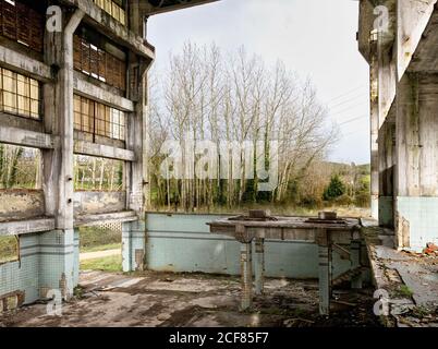 Rovine di vecchia officina industriale trascurata con muri di scabvicino e. Banco di lavoro situato contro la foresta di primavera senza frondosi nelle Asturie in Spagna Foto Stock