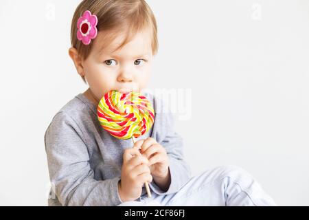 Bambina che mangia lecca. Felici i bambini con una grande caramella deliziosa. Ritratto di bambina su sfondo bianco Foto Stock