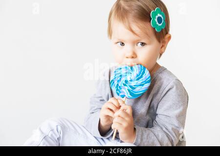 Bambina che mangia lecca. Felici i bambini con una grande caramella deliziosa. Ritratto di bambina su sfondo bianco Foto Stock