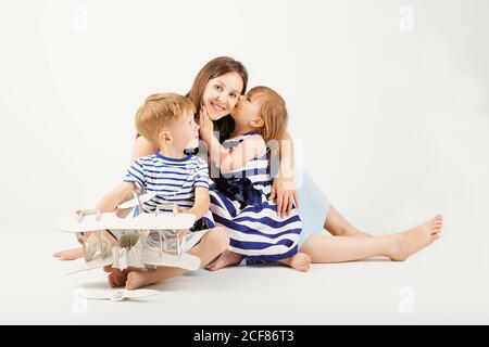 Ritratto di una madre felice e dei suoi due bambini - ragazzo e ragazza. Famiglia felice su sfondo bianco. Bambini piccoli che baciano la madre. Bambini w Foto Stock