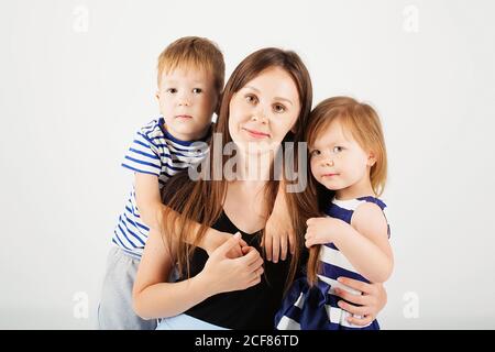 Ritratto di una madre felice e dei suoi due bambini - ragazzo e ragazza. Famiglia felice su sfondo bianco. Bambini piccoli che baciano la madre. Bambini w Foto Stock