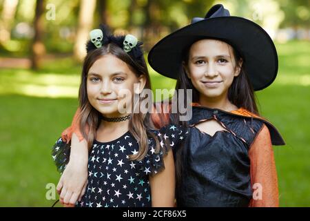 Ritratto di due ragazze in costumi di Halloween sorridenti alla macchina fotografica in piedi all'aperto Foto Stock